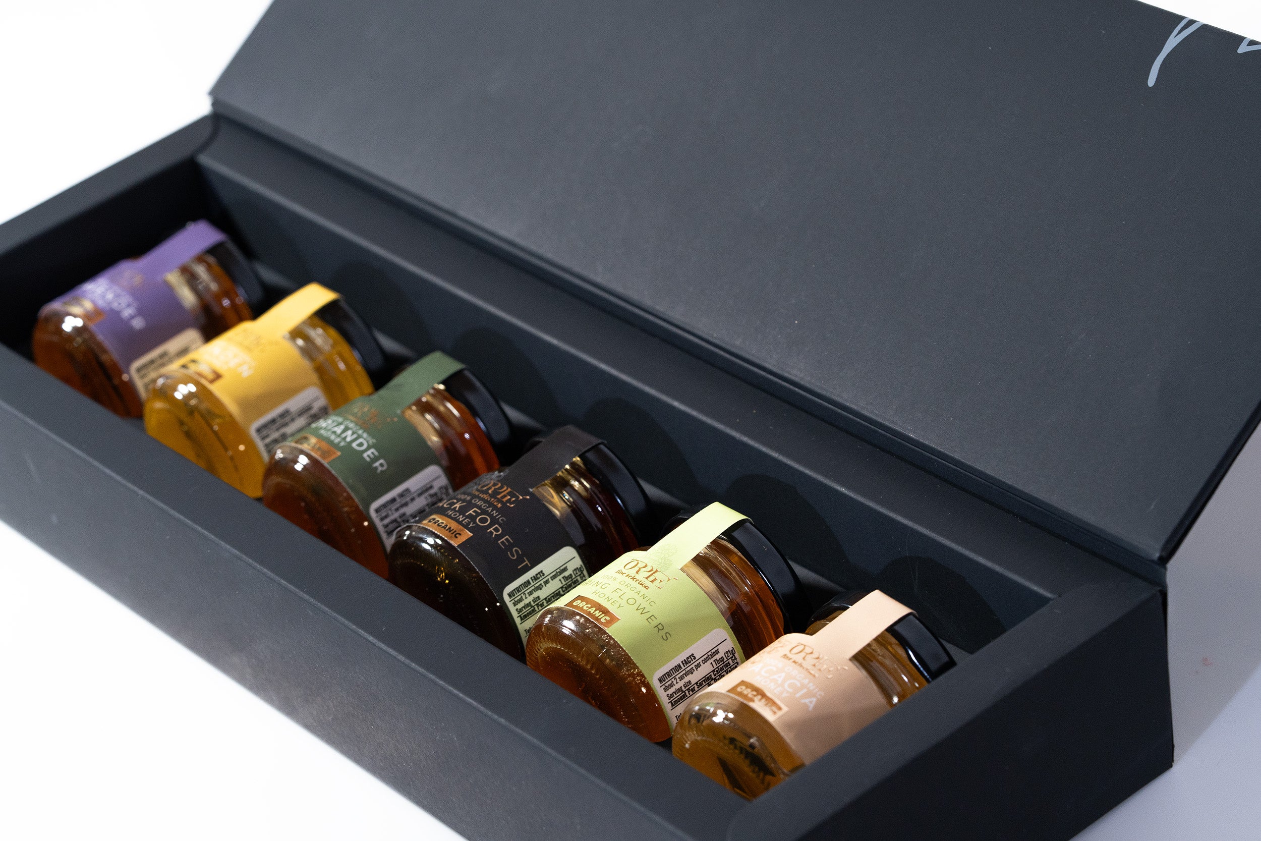 Set of small bottles with colorful labels in a black box, featuring lavender syrup, clover honey, lavender simple syrup, and purple honey.