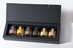 Set of six small jars with labels in a black display box on a white background, featuring lavender syrup and clover honey.