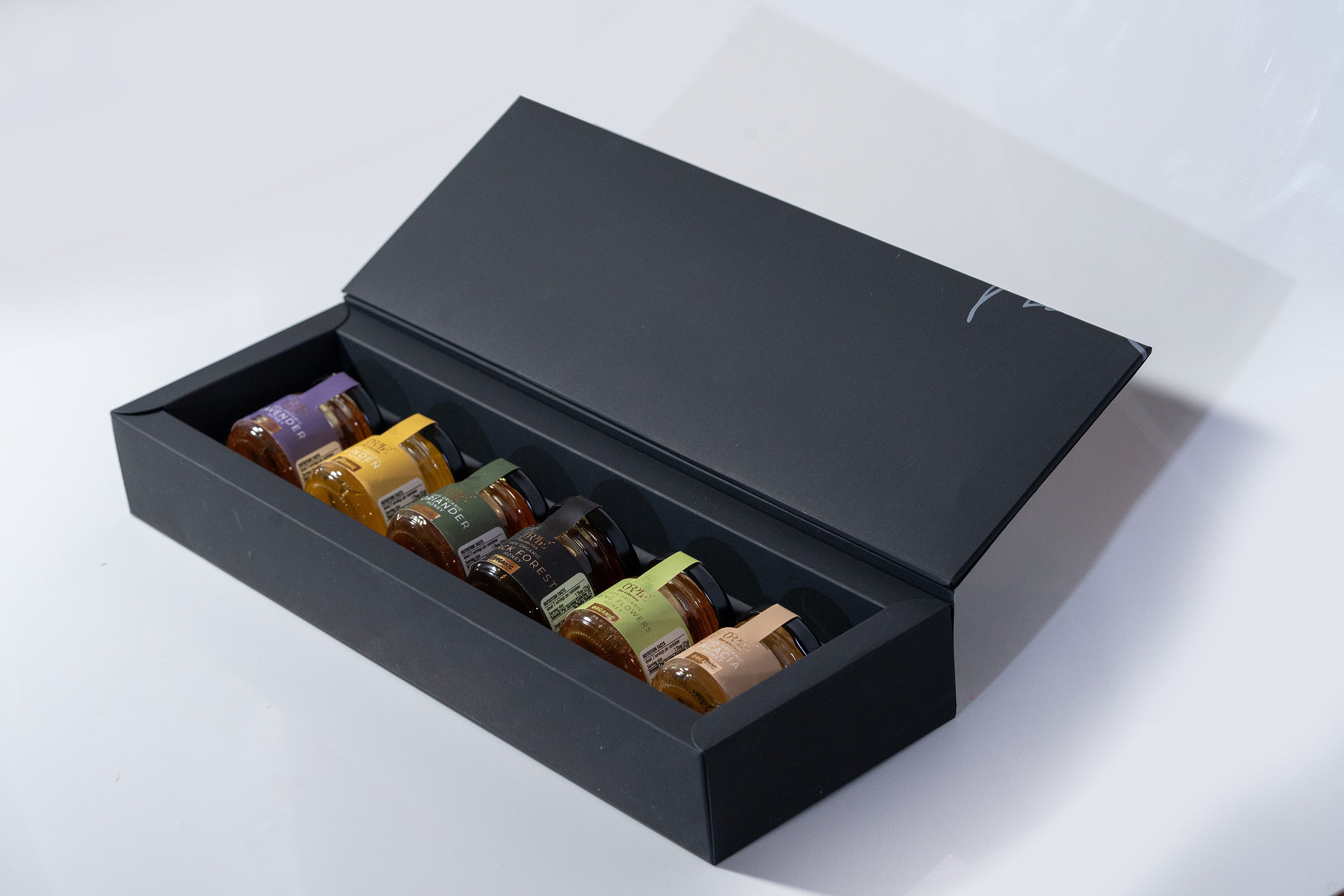 Open black box with small bottles arranged inside on a white background, showcasing lavender simple syrup and purple honey.