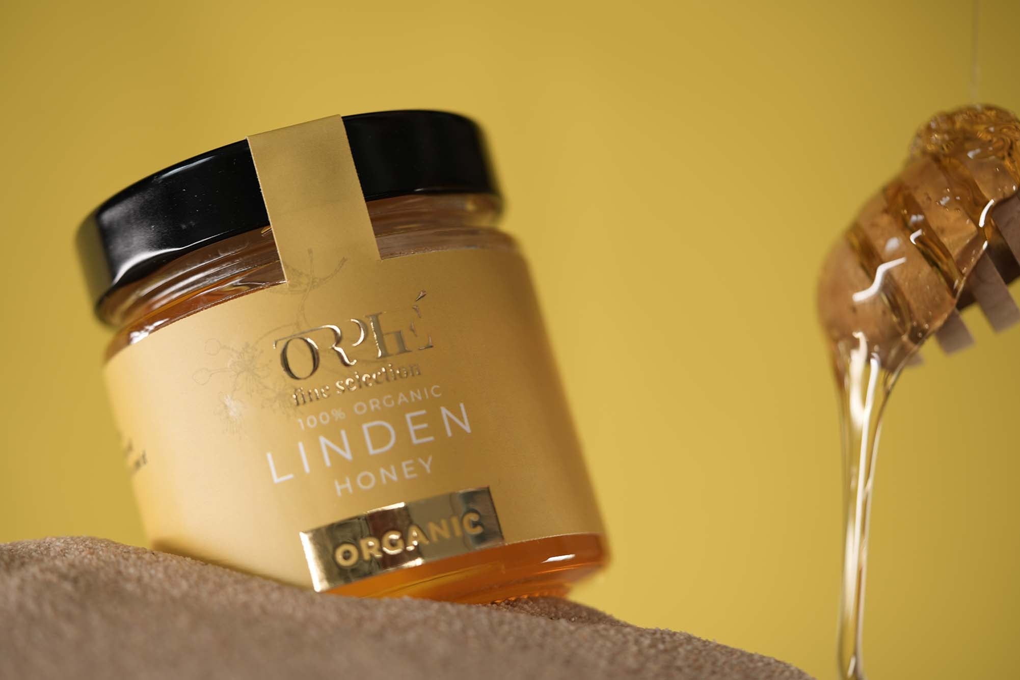 Jar of organic linden honey with a spoonful of honey on a yellow background