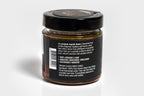 Clear glass jar filled with golden honey, topped with a sleek black lid. The jar is photographed against a clean white background, highlighting the rich color of the honey and the minimalist packaging.
