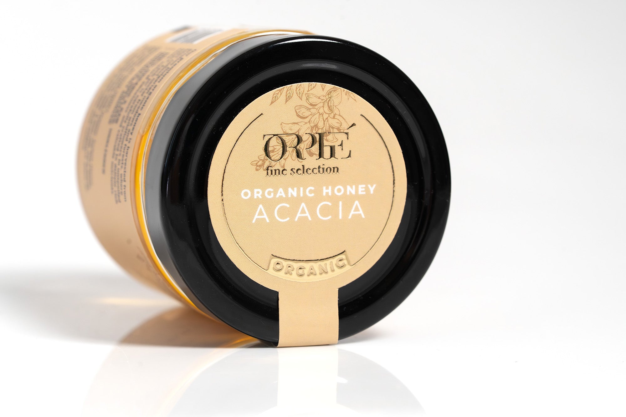 Clear glass jar of Orlé organic honey with a sleek black lid, filled with rich golden amber honey. The jar features a clean, minimalist label showcasing the Orlé brand, and is photographed against a bright white background for a fresh, professional presentation.
