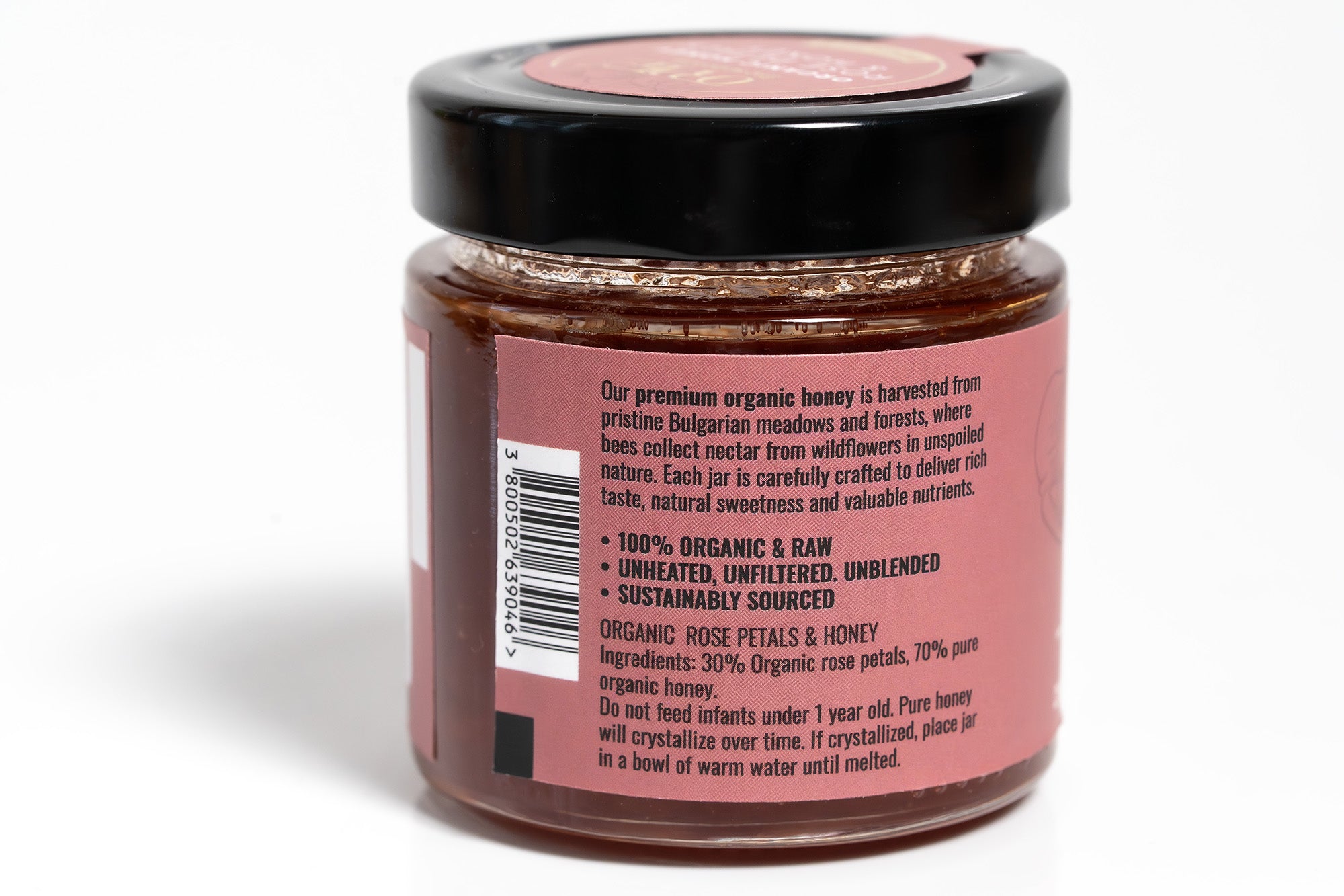 Clear glass jar filled with golden honey, featuring a vibrant pink label with elegant typography. The jar is photographed against a clean white background, highlighting the rich color of the honey and the eye-catching label design.