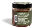 Clear glass jar filled with golden honey, featuring a green label with natural design elements. The jar is photographed against a clean white background, emphasizing the vibrant label and the rich color of the honey inside.