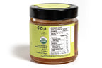 Clear glass jar of honey showing the back side with a detailed nutrition label and ingredient list. The golden amber honey is visible through the jar, and the product is placed against a clean white background for a crisp, professional presentation.