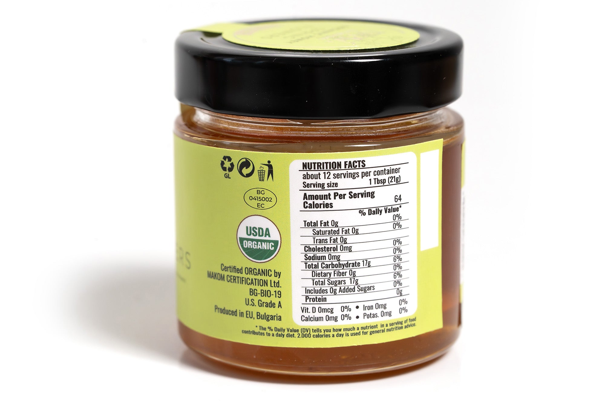 Clear glass jar of honey showing the back side with a detailed nutrition label and ingredient list. The golden amber honey is visible through the jar, and the product is placed against a clean white background for a crisp, professional presentation.