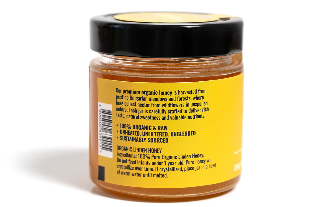 Glass jar of honey filled with golden amber honey, featuring a bright yellow label and a sleek black lid. The jar is photographed against a clean white background, emphasizing the vibrant label and the rich color of the honey.