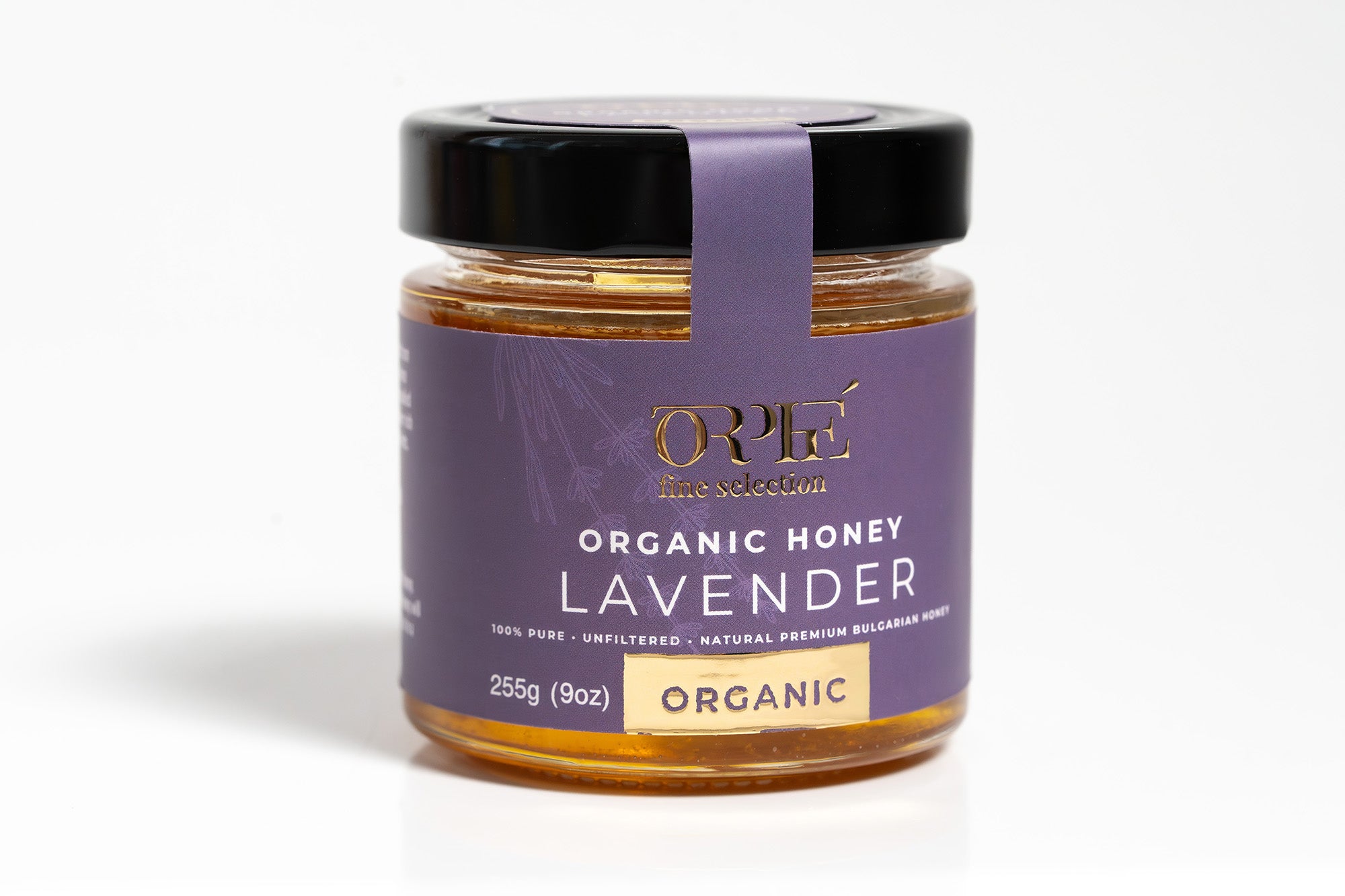 Glass jar of premium organic lavender honey with a deep purple label featuring elegant floral illustrations and gold foil detailing. The label includes product name and branding in a stylish serif font. The jar is sealed with a gold metal lid, and the honey inside has a rich amber color. The product is photographed against a clean white background for a minimal, modern look — ideal for natural or artisanal food product listings.