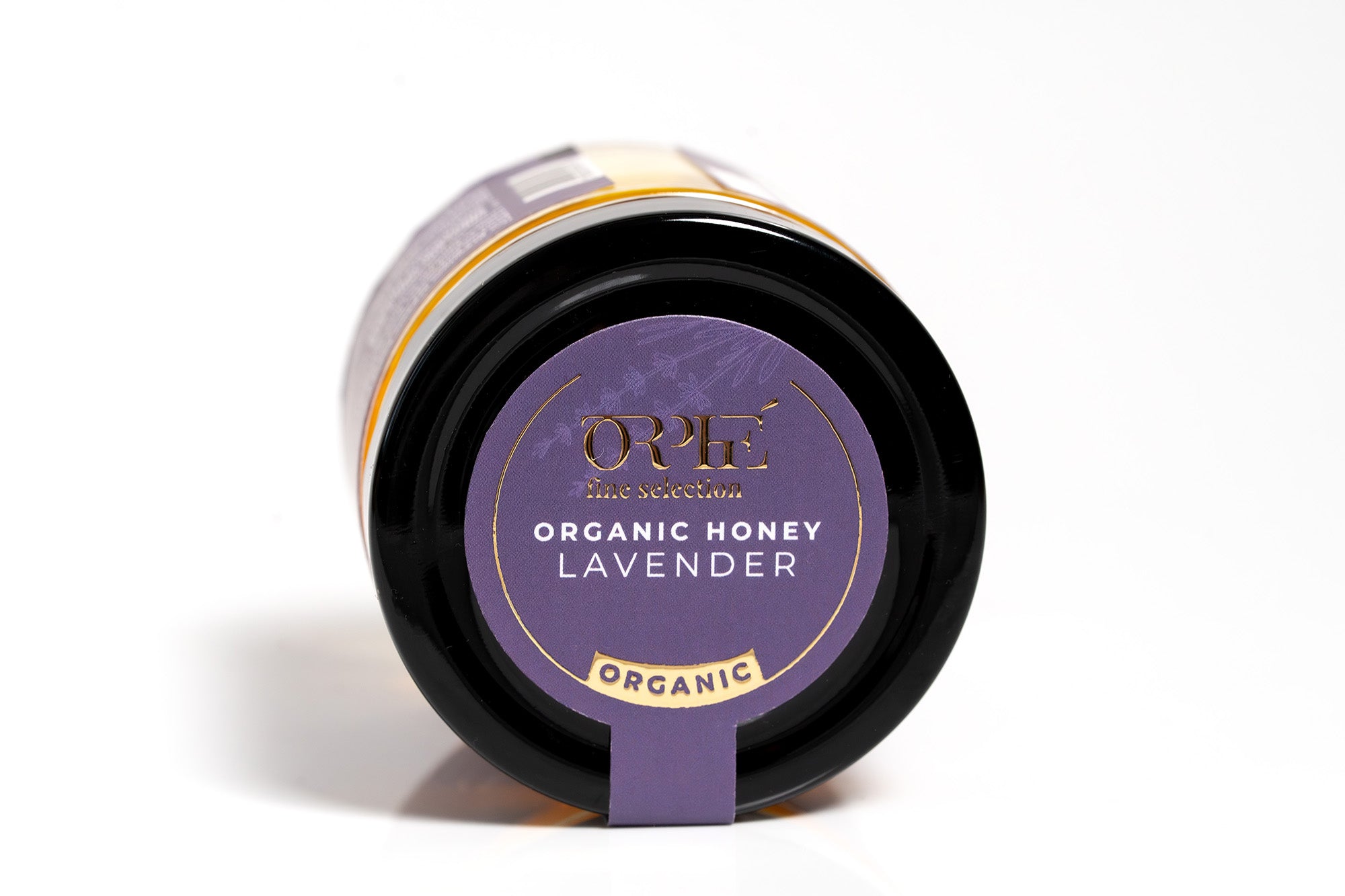 "Glass jar of organic lavender-infused honey with a golden amber color, photographed on a clean white background. The jar features a minimalistic design, highlighting the natural and artisanal quality of the product.